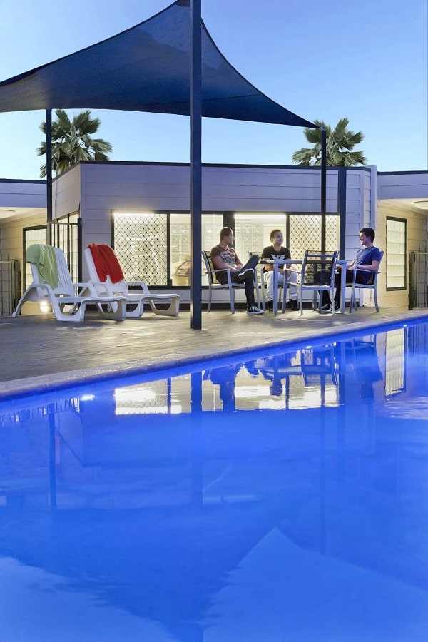 3 men sitting and talking beside a swimming pool of the Mont Clare Apartments.